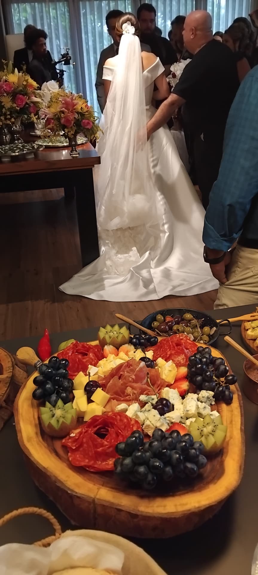 Tábua de queijos, embutidos e frutas montada em casamento, com a noiva ao fundo