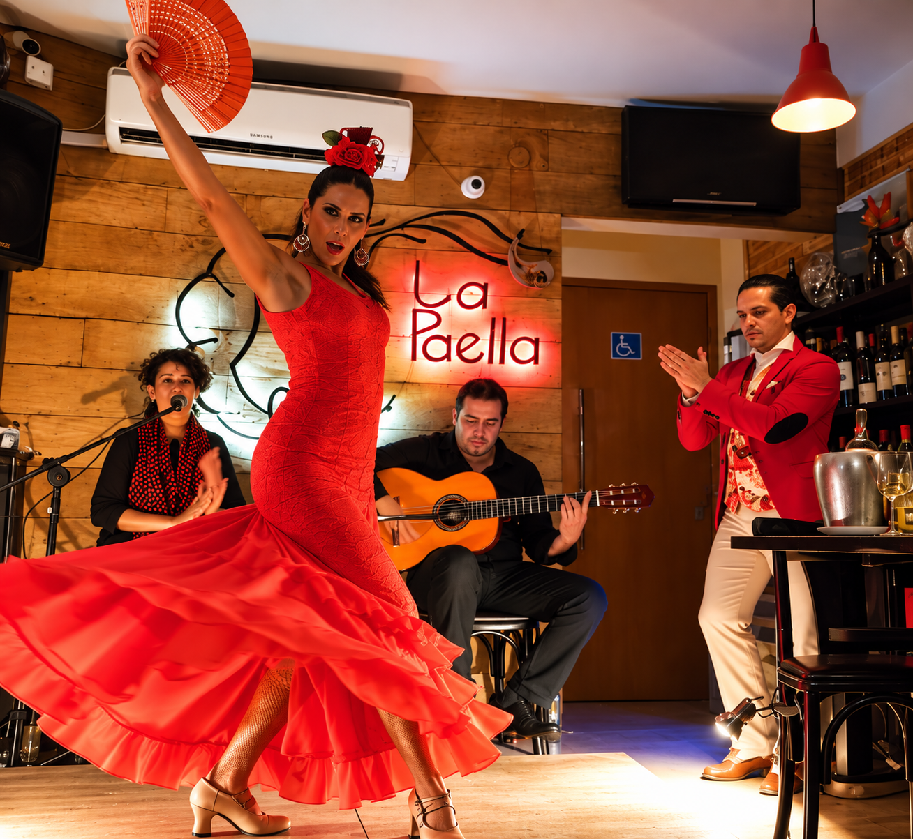 Bailaora de vestido vermelho com os braços erguidos, de costas para a câmera, em jantar com convidados à mesa