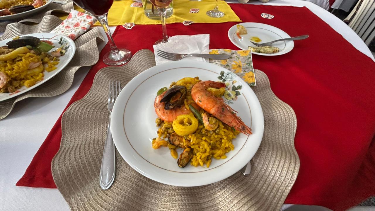 Prato individual de paella de frutos do mar servido na mesa do evento, com camarão, mexilhões e lula