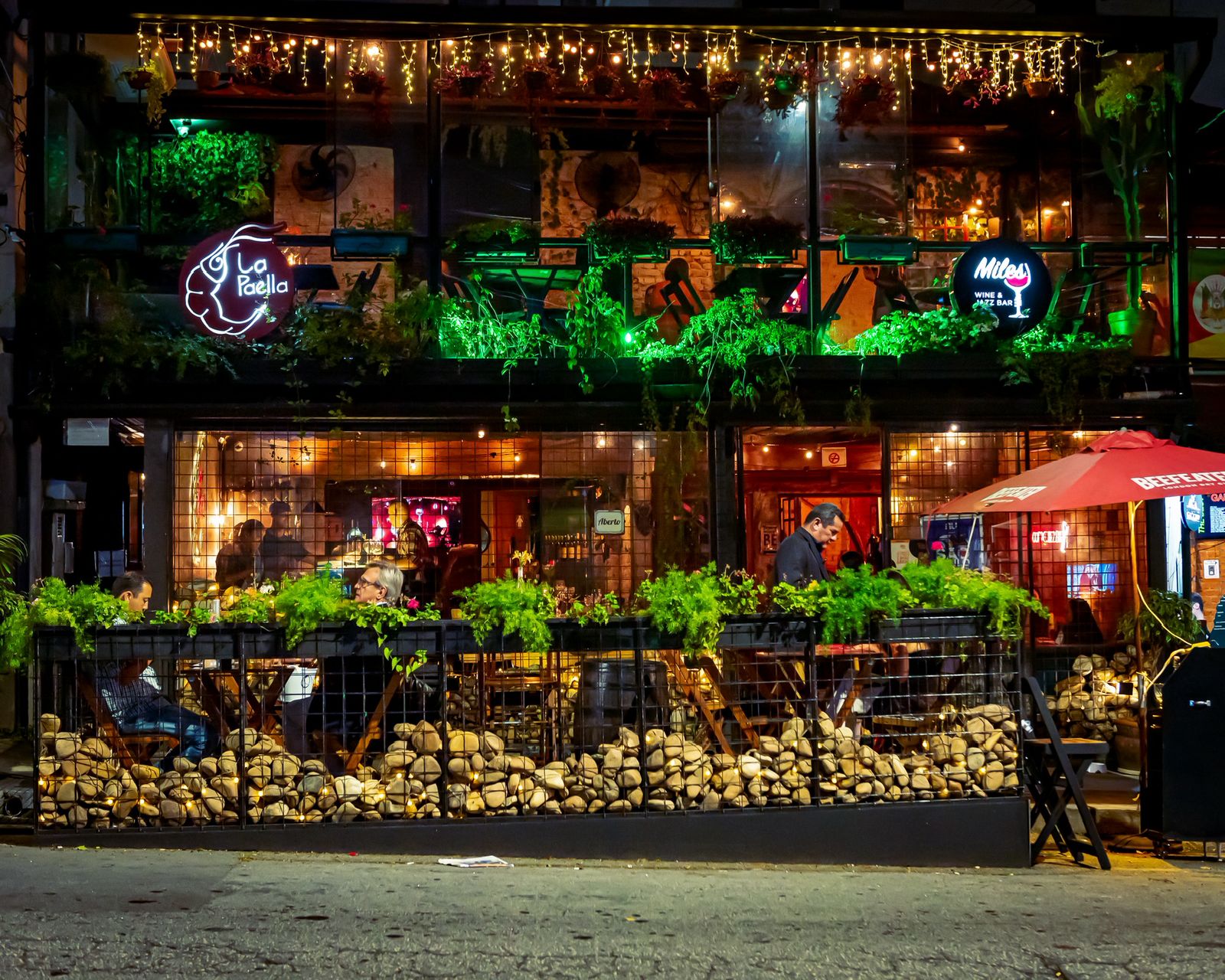 Fachada do restaurante La Paella à noite, com o letreiro neon e o salão iluminado