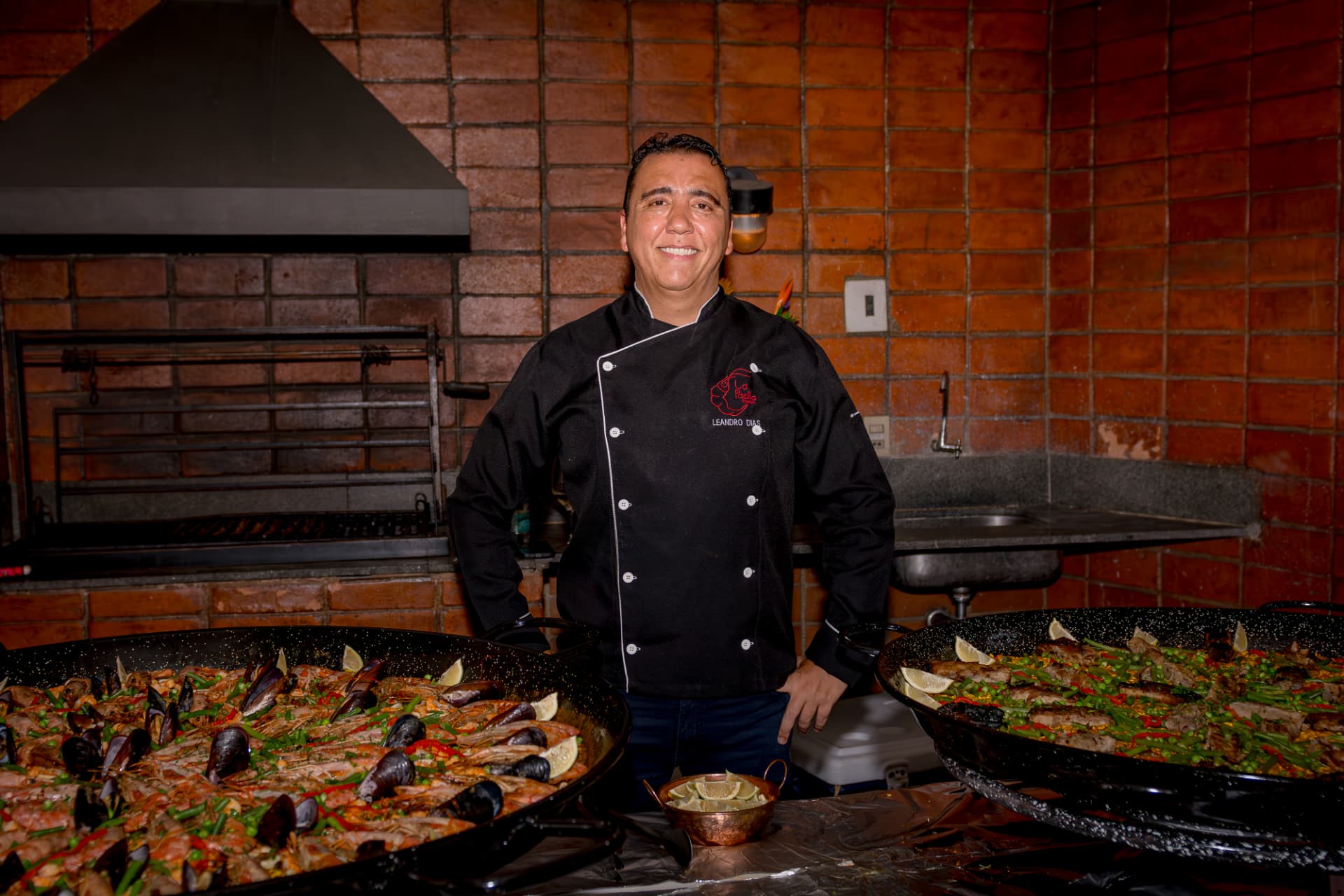 Leandro Dias, fundador do La Paella, diante de duas paelleras no restaurante