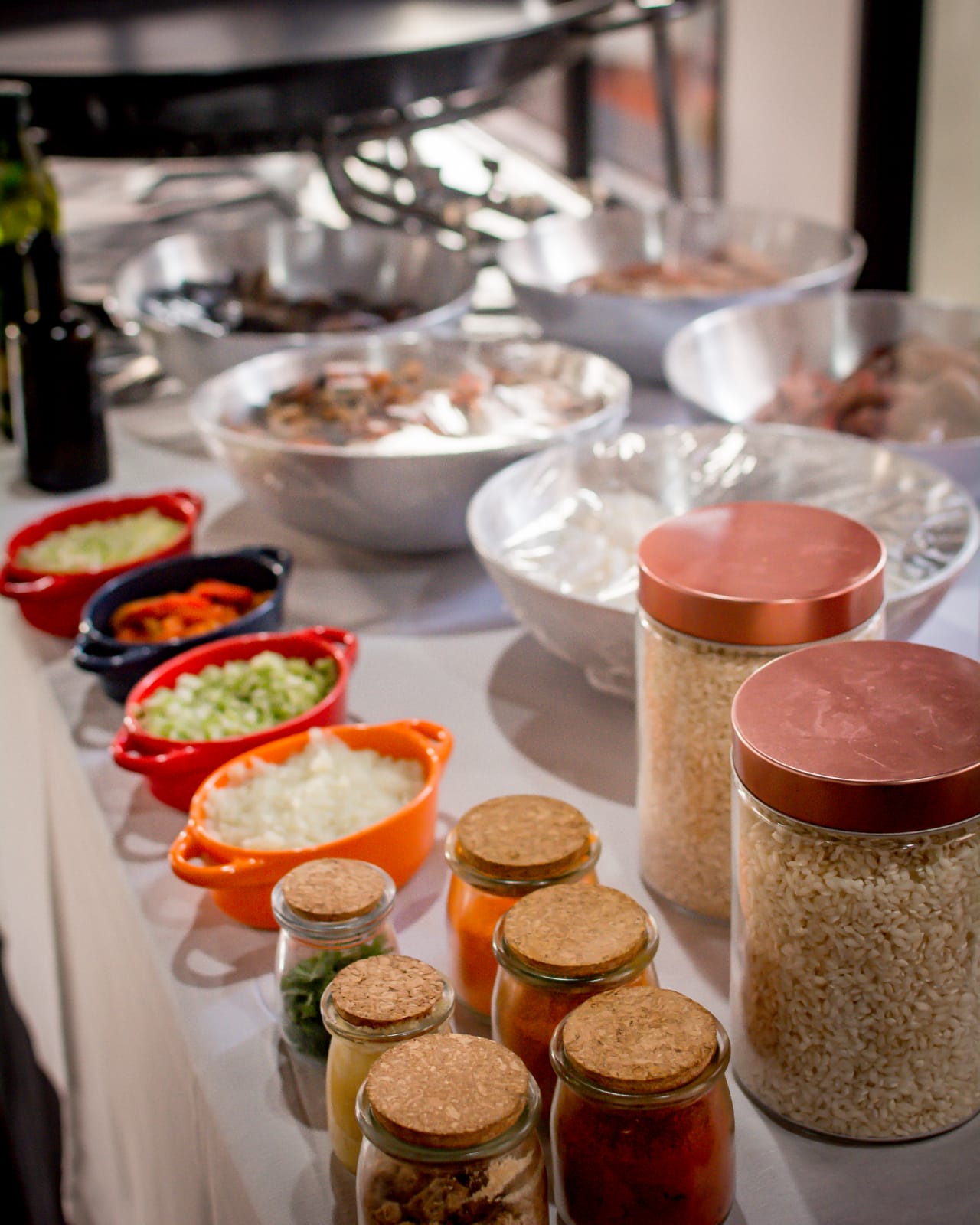 Bancada de preparo com temperos, arroz e legumes cortados diante da paellera
