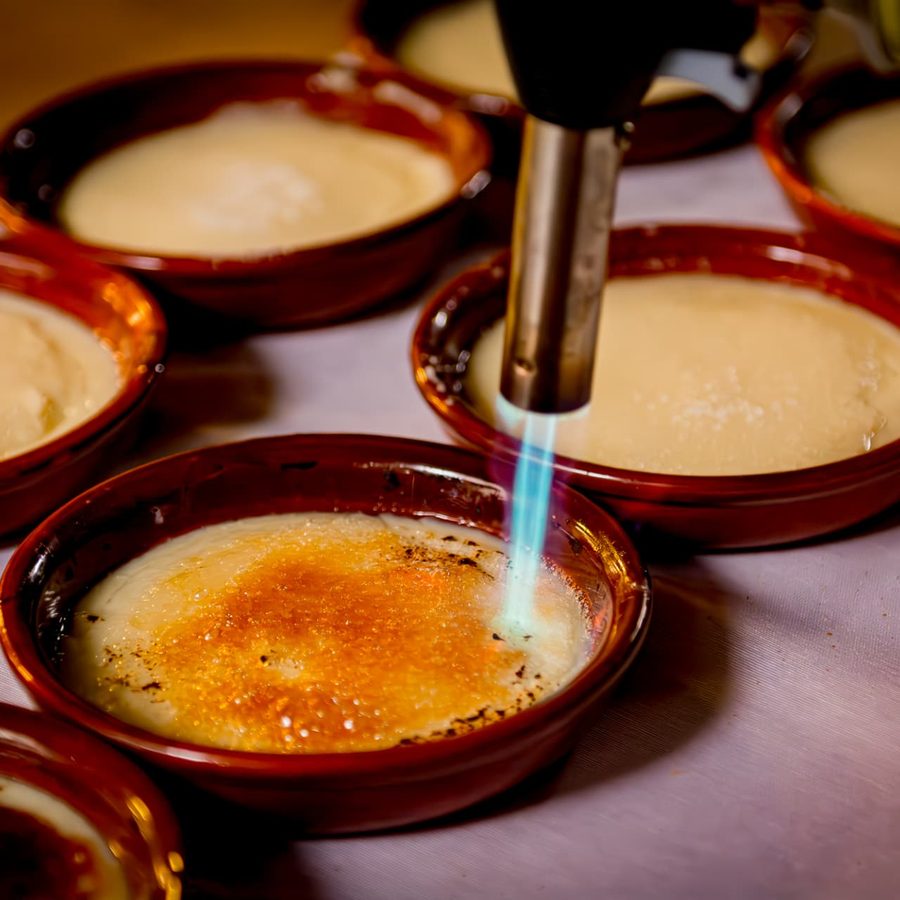 Crema catalana sendo caramelizada com maçarico em cumbucas de terracota